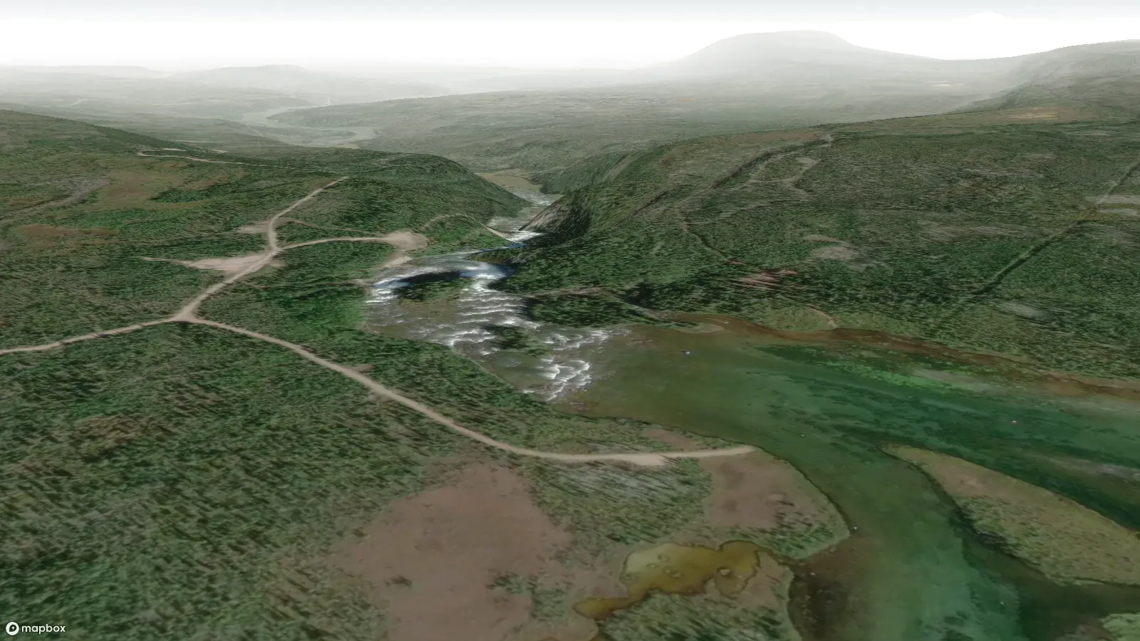 Satelite view of the Nàı̨lı̨ı̨ (Whatì Falls) area. The wide Lac La Martre river narrows and plunges over a steep drop, with white rapids visible from the air. A utility road is visible on the left shore of the river, and portage footpaths are visible on the right shore of the river.