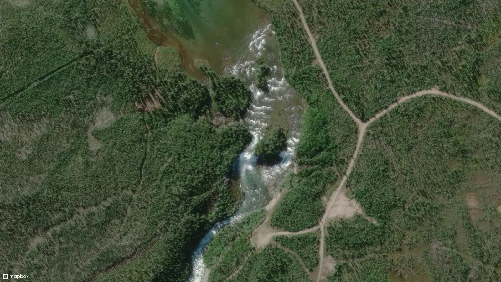 La large rivière du lac La Martre se rétrécit et plonge sur une pente raide, avec des rapides blancs visibles depuis les airs. Une route de service public est visible sur la rive droite de la rivière, et des sentiers de portage sont visibles sur la rive gauche de la rivière.