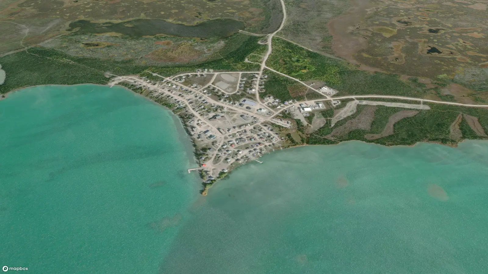 Satellite view of the community of Whatì on the shores of Lac La Martre. Dirt roads criss cross between colorful buildings that dot the town.