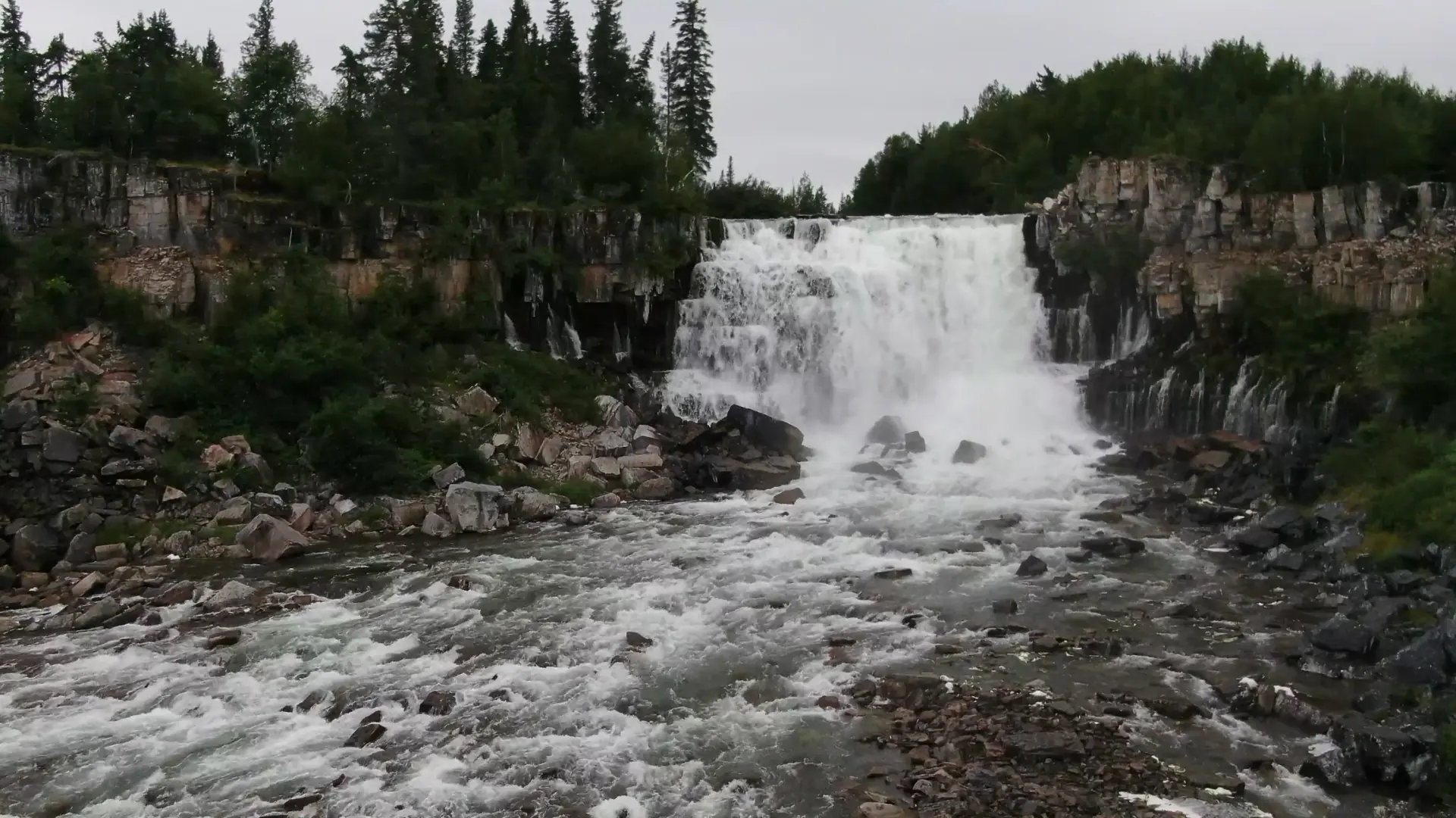 Vue aérienne de la rivière La Martre plongeant sur l'une des deux chutes de 15 mètres qui forment les Nàı̨lı̨ı̨ (chutes de Whatì). De plus petits cours d'eau se déversent des parois rocheuses de chaque côté de la rivière.